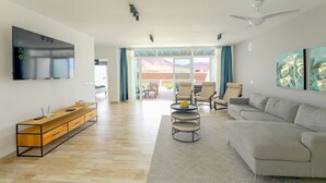 Een ruime woonkamer met een grote flatscreen-tv, een bank, een salontafel en een balkon met uitzicht op de bergen.