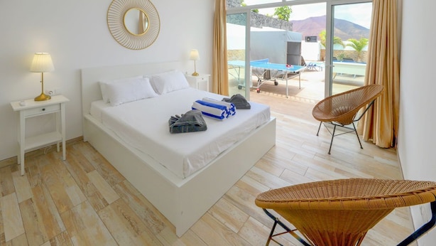 Een slaapkamer met een bed, nachtkastjes, een stoel en uitzicht op een buitenzwembad.