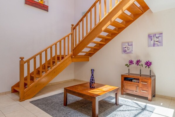 Eine Holztreppe führt zu einer oberen Etage, ein kleiner Holztisch mit einer Vase und ein Holzschrank mit Blumen.