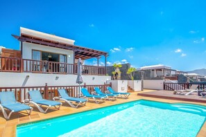 A pool area with lounge chairs and a building with a balcony. - Lanzarote Lauren - Four Bedroom Villa, Sleeps 9 (Playa Blanca)