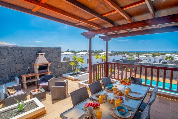 An outdoor patio with a stone wall, a grill, wicker furniture, and a table set for breakfast.
