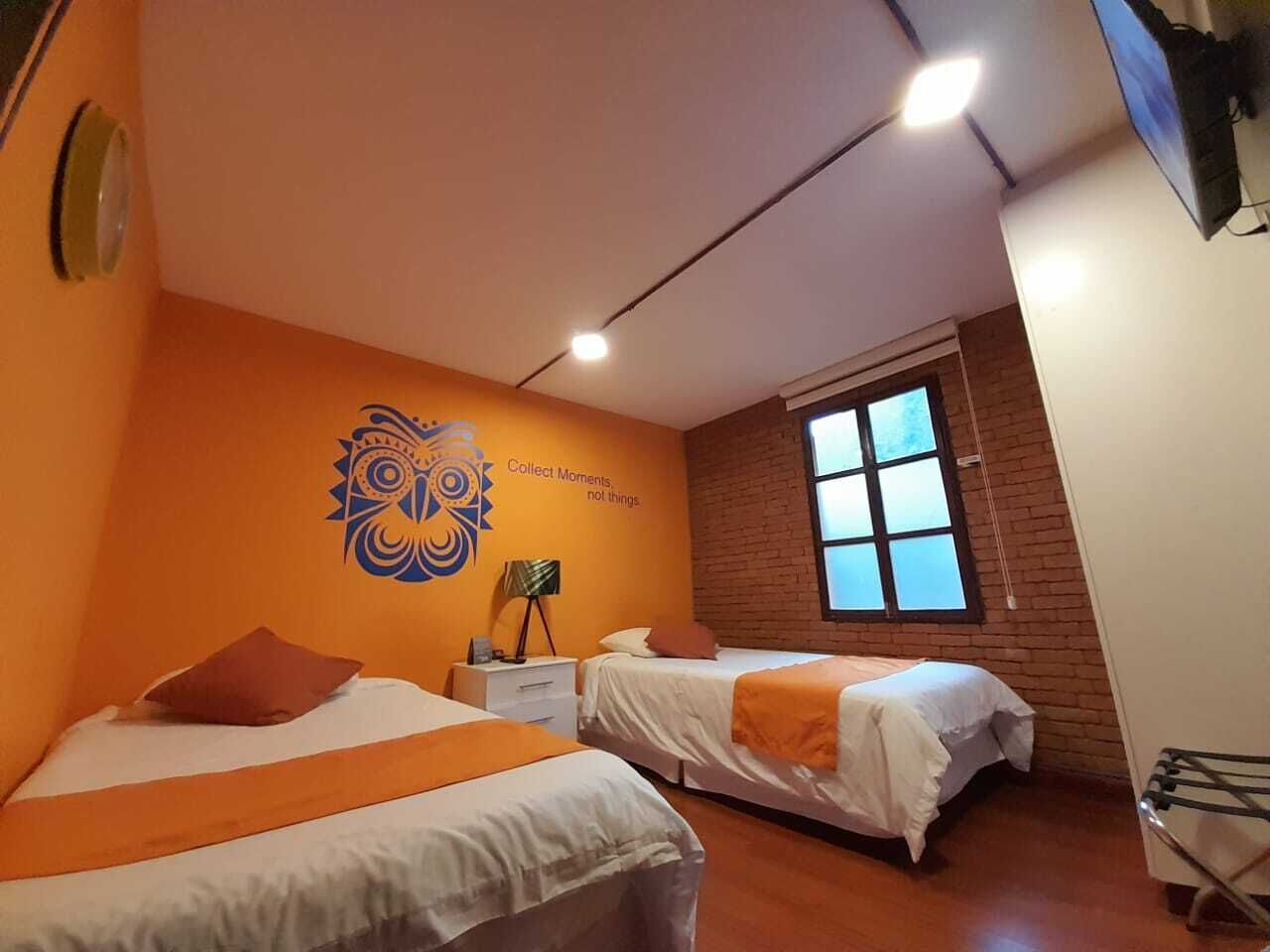 A room with two beds, a brick wall, a window, and a wall decoration.