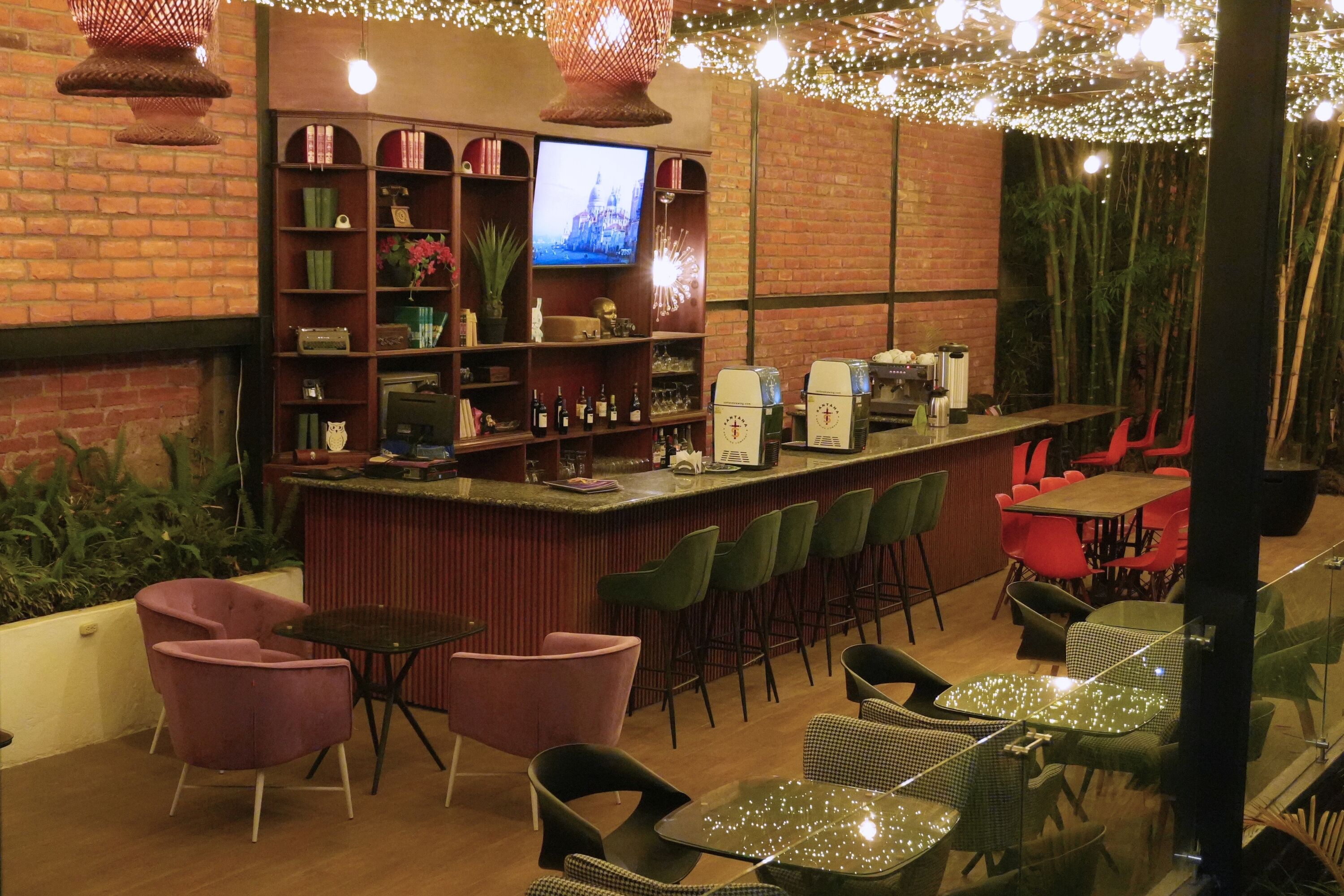 Un espace bar équipé d’un téléviseur, d’étagères contenant des livres et des objets décoratifs, et de différents types de sièges, notamment des tabourets de bar et des tables.