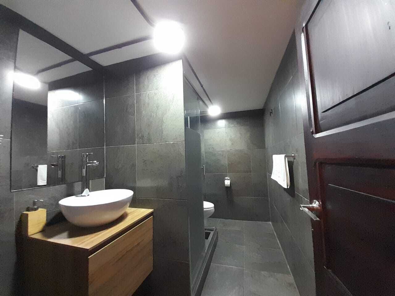 A modern bathroom with a large white sink, dark tiled walls, and a wooden vanity.