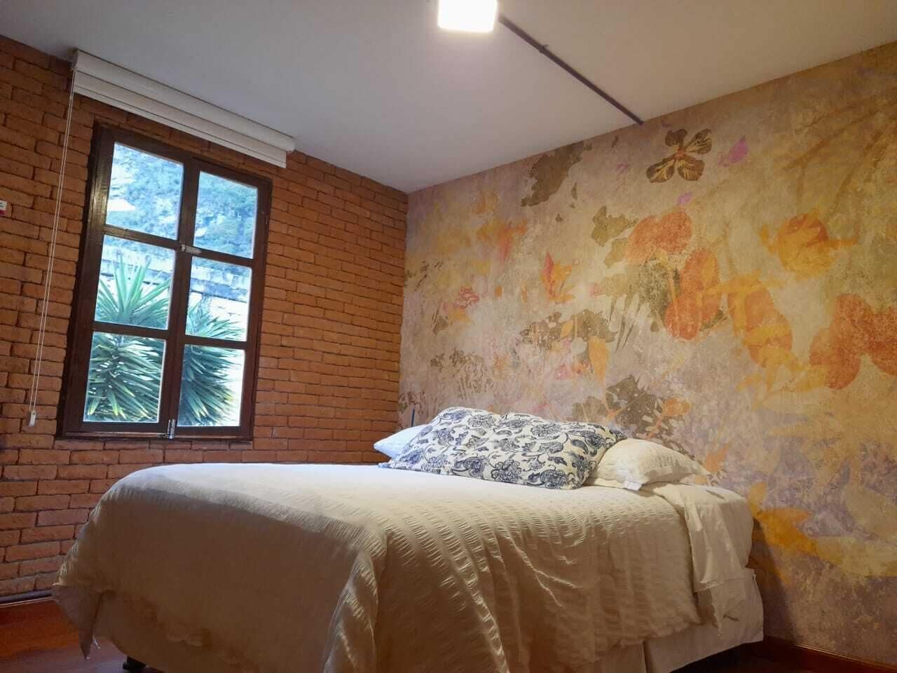 Un dormitorio con pared de ladrillo, ventana grande y papel tapiz floral.