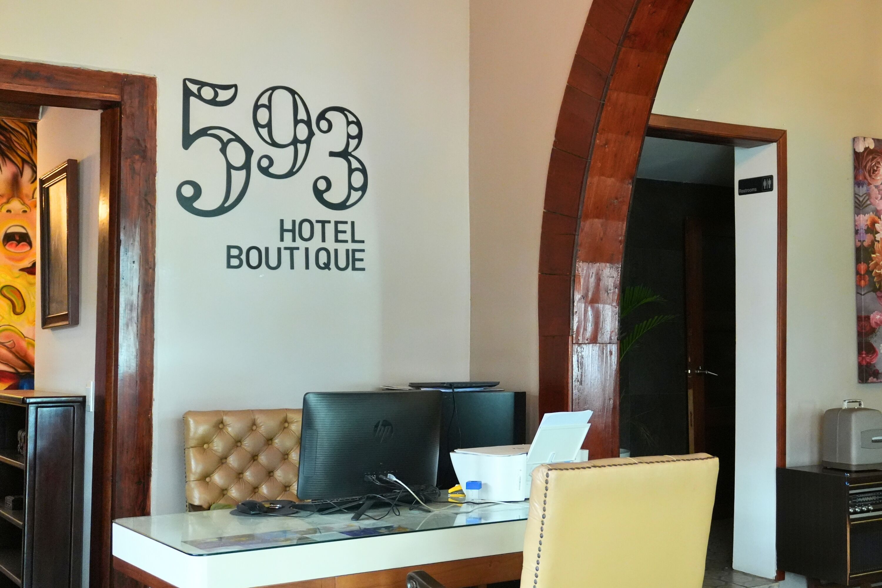 A reception desk with a sign reading '593 HOTEL BOUTIQUE,' a laptop, a telephone, and a cushioned chair.