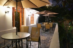 Un patio al aire libre con mesas y sillas redondas, sombrillas y piso de baldosas.