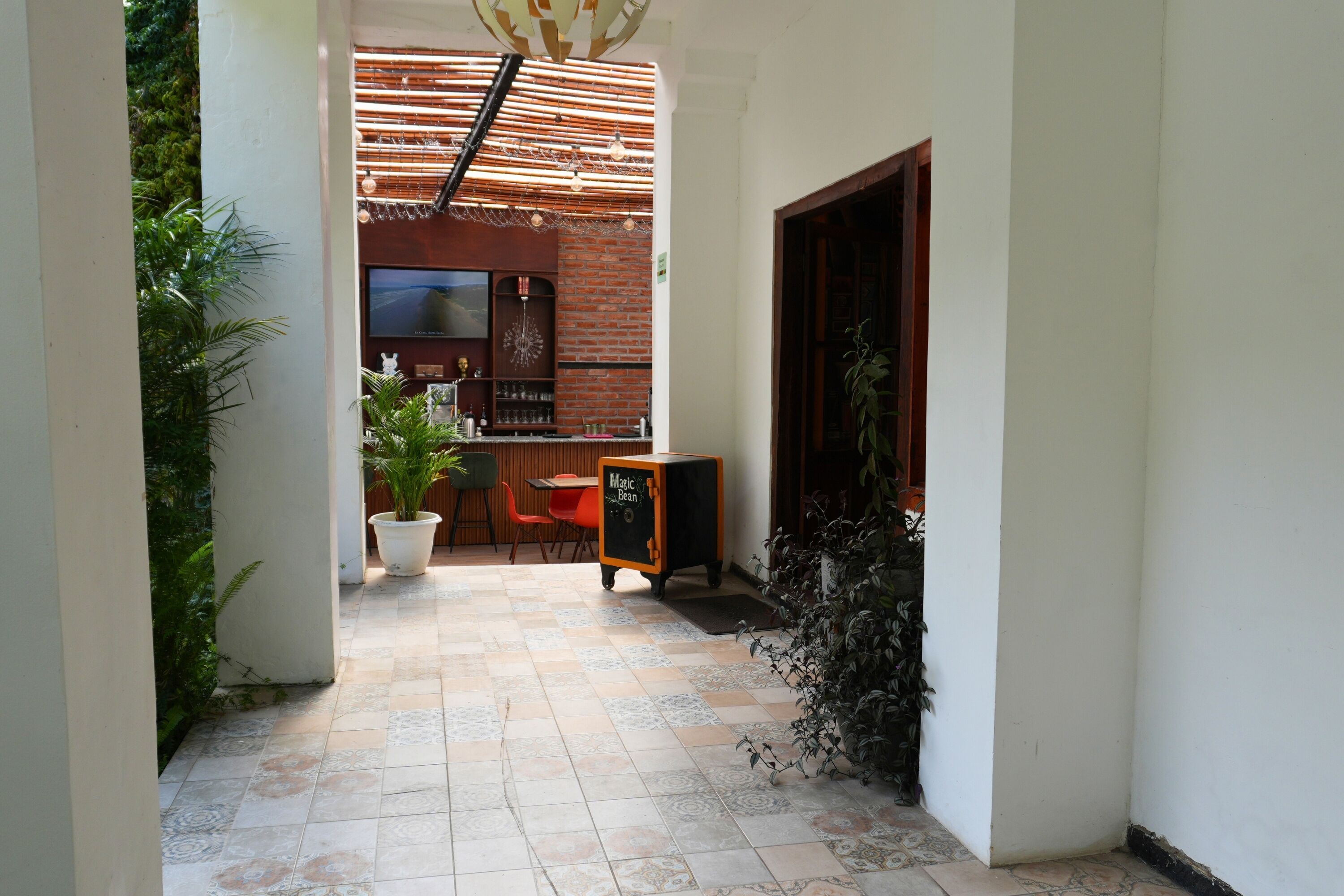 A corridor with a tiled floor, a brick wall, a wooden door, and a bar area with a television and shelves.