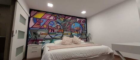 A bedroom with a bed, a nightstand, a dresser, and a colorful abstract mural on the wall.