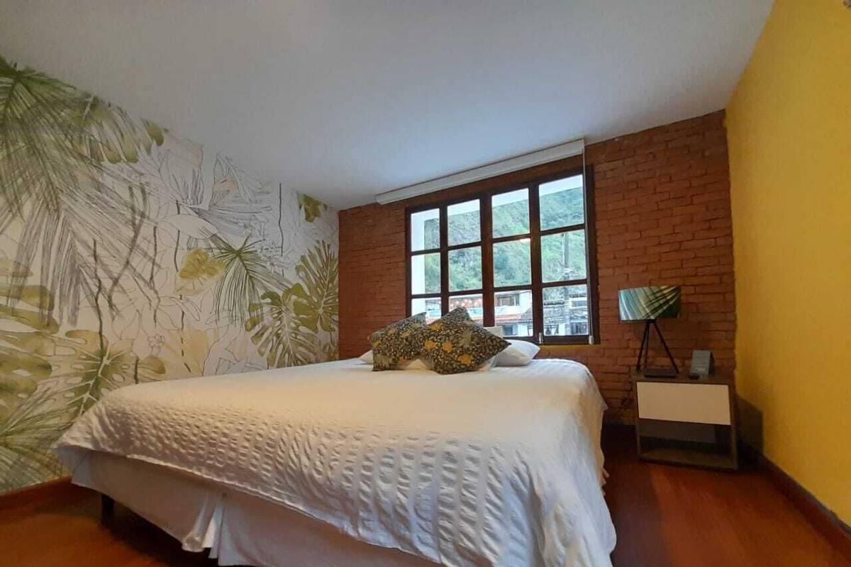 A bedroom with a large bed, a brick wall, a window, and a plant.