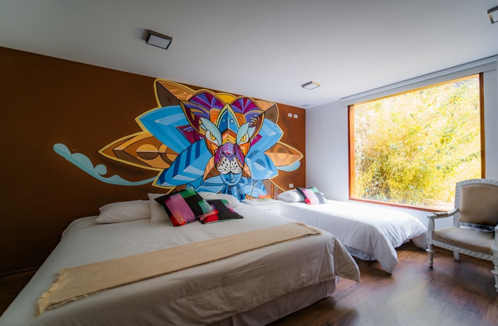 Habitación de hotel con dos camas, un cuadro abstracto grande en la pared y vista a los árboles por la ventana.