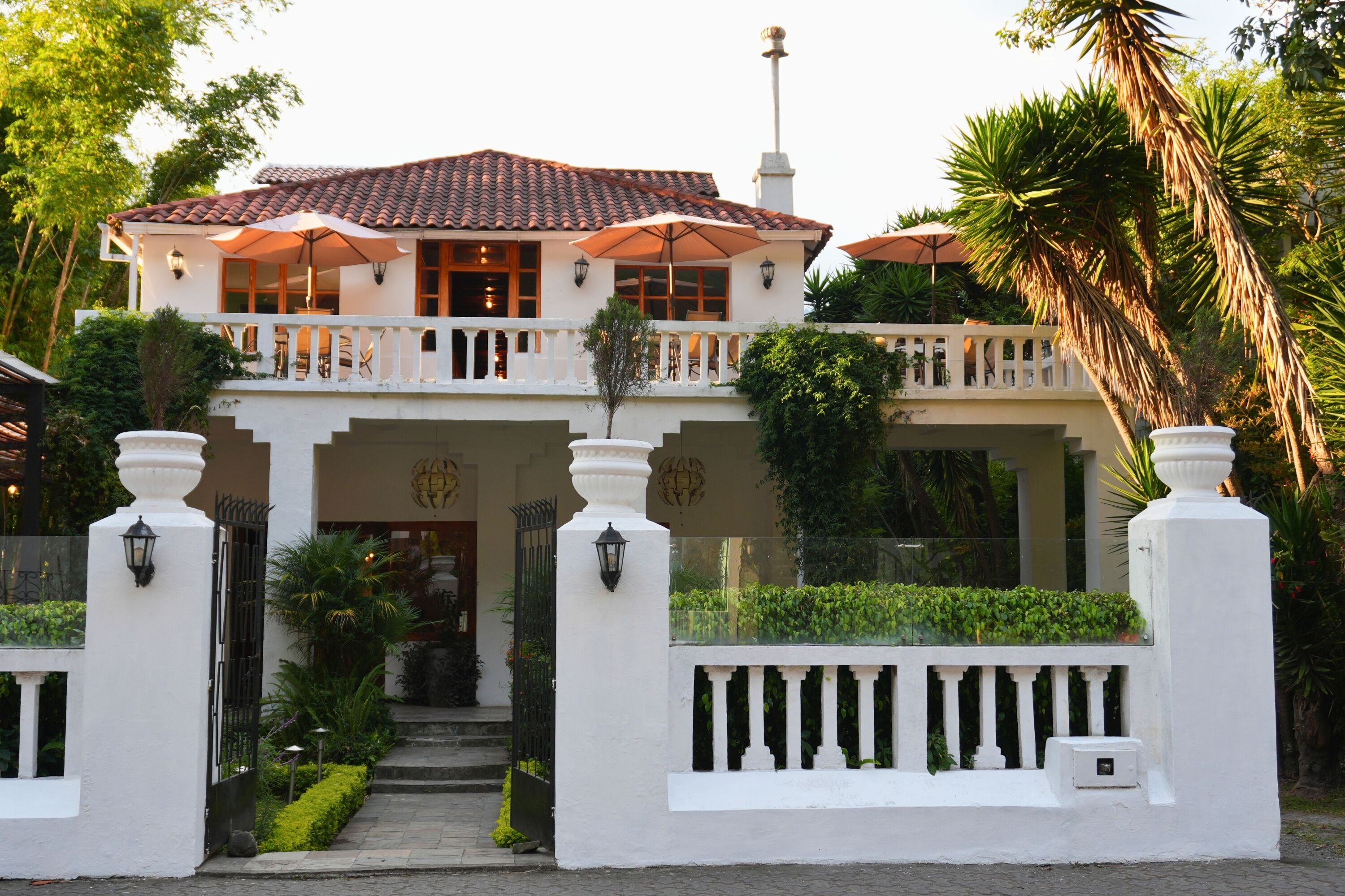 A two-story house with a balcony, a white fence, and a garden.