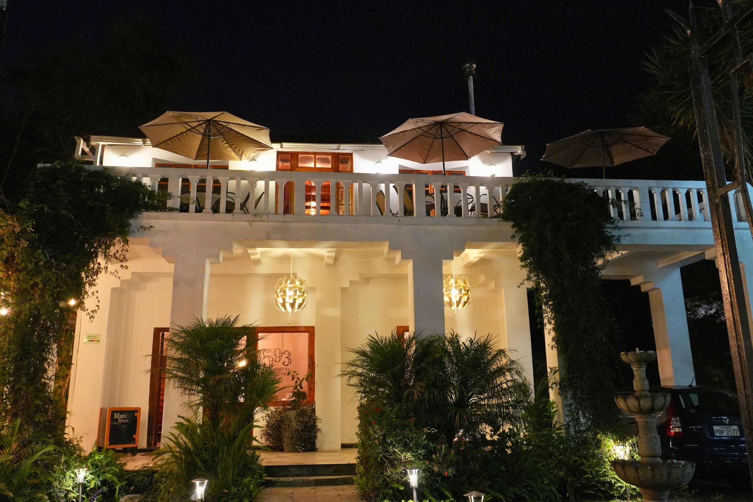 Un hotel con fachada blanca, varias sombrillas y una entrada bien iluminada.