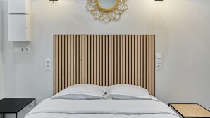 A modern bedroom with a wooden slat headboard, a round mirror, and two bedside lamps. - Charon 4 - Studio Apartment, Sleeps 2 (Paris)