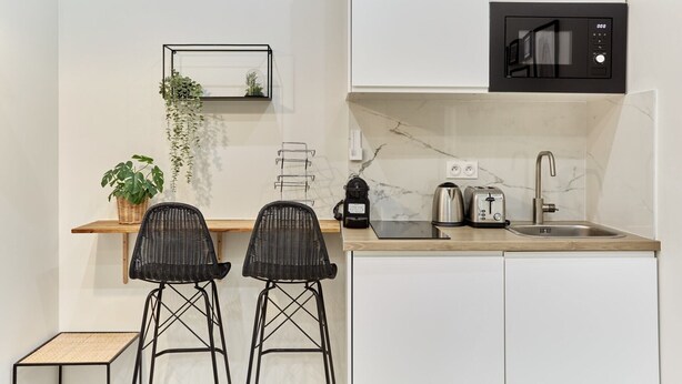A modern kitchen with white cabinets, a black microwave, a sink, and two black bar stools. - Charon 4 - Studio Apartment, Sleeps 2 (Paris)