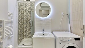 A modern bathroom with a shower, a sink, a mirror, and a washing machine. - Charon 4 - Studio Apartment, Sleeps 2 (Paris)