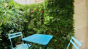 Un petit espace extérieur aménagé avec une table bleue et deux chaises bleues, entouré d’un feuillage verdoyant et luxuriant et de diverses plantes.