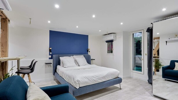 Une chambre moderne avec un lit, un bureau et une chaise. Une porte-fenêtre coulissante donne accès à un balcon.