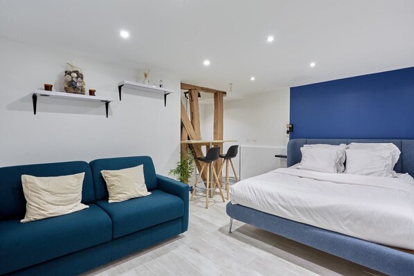 Une chambre moderne avec un canapé bleu, un lit avec une literie blanche et une petite table avec des chaises.
