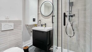 Une salle de bain moderne avec une douche à l’italienne en verre, un lavabo blanc avec un miroir au-dessus et un meuble noir en dessous.