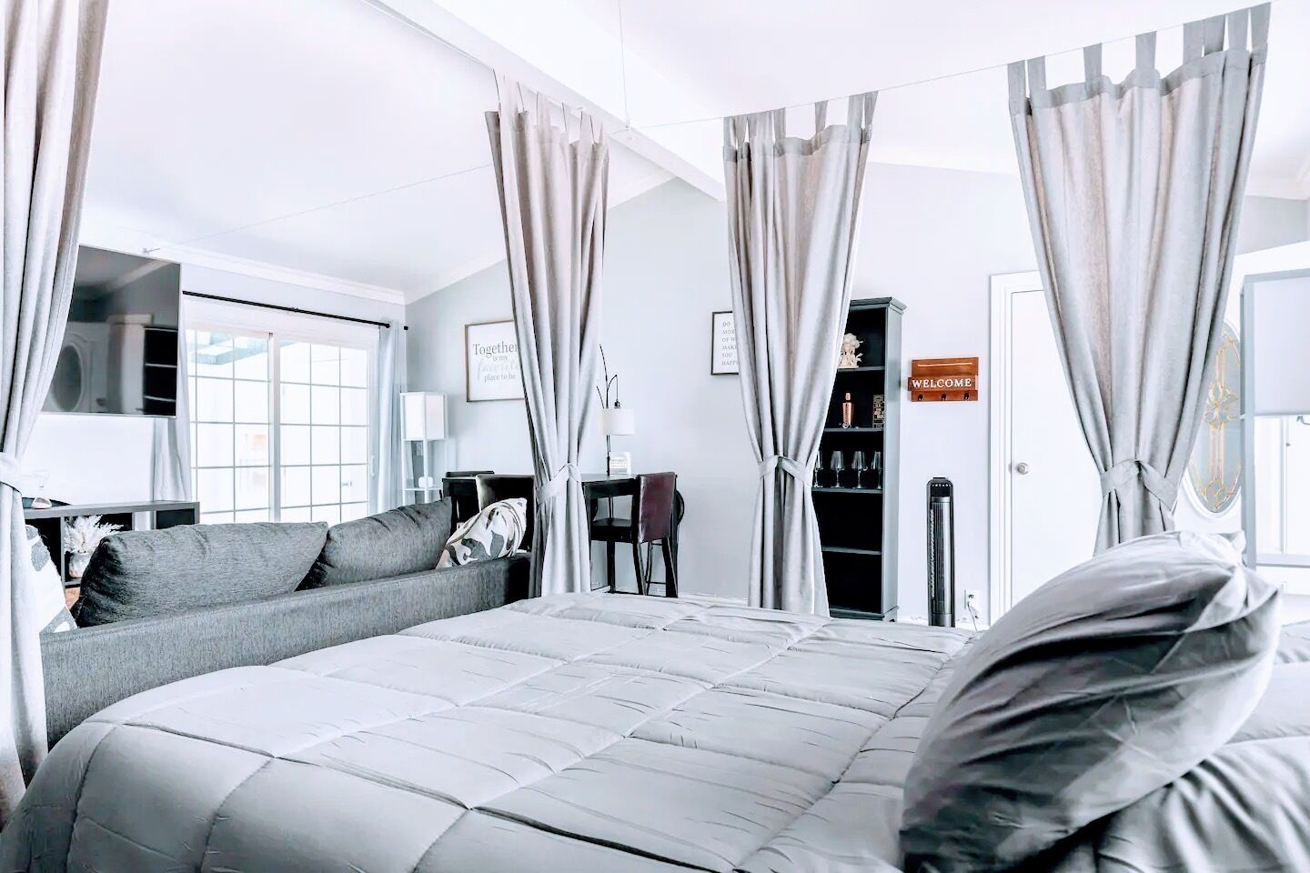 Una habitación de hotel moderna con una cama grande, cortinas grises, un sofá, un escritorio y una estantería.