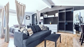 Ein modernes Wohnzimmer mit grauem Sofa, einem schwarzen Couchtisch und Holzboden. Es gibt eine Küchenzeile mit schwarzer Arbeitsplatte und Schränken.