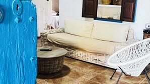 A living room with a beige sofa, a white wicker chair, a small round table, and a blue door. - Can Pep Tauet Formentera, al Centro de la Isla, muy Bien Comunicada (FORMENTERA)