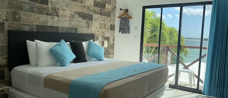 Un dormitorio con una cama grande, cabecera de madera, vista al océano y un balcón con barandilla.