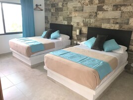 Dos camas con ropa de cama color beige y azul, una pared con diseño de piedra y una ventana con cortinas azules.