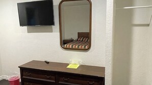A room with a dark wooden dresser, a mirror, and a flat-screen TV mounted on the wall. - Welcome Inn & Suites (Anaheim)