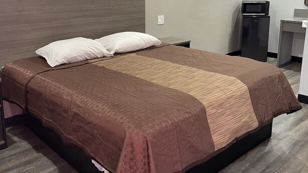 A hotel room with a large bed, a bedside table, a microwave, and a small desk with a chair. - Welcome Inn & Suites (Anaheim)