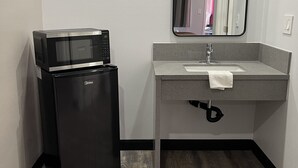 A compact bathroom with a built-in microwave, a sink with a towel, and a mirror. - Welcome Inn & Suites (Anaheim)
