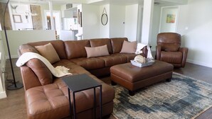 Ein modernes Wohnzimmer mit einem braunen Ledersofa, passendem Hocker und einem kleinen schwarzen Couchtisch.