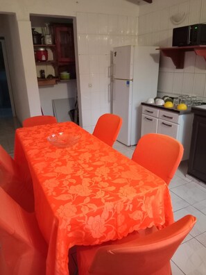 Un coin repas avec une table recouverte d’une nappe à motifs floraux, entourée de chaises orange.