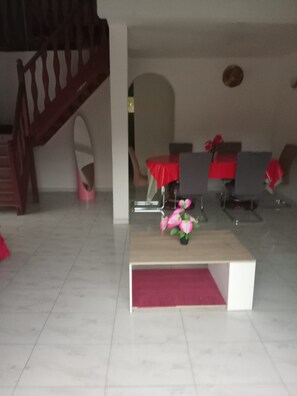 A modern living room with a staircase, a dining area with red tablecloths, and a small table with a vase of flowers.