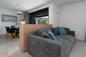 Ett modernt vardagsrum med en grå soffa, ett träbord och en matplats med ett svart bord och stolar.