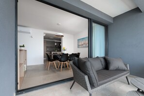 Ett modernt vardagsrum med en grå soffa, en matplats med svarta stolar och ett kök i bakgrunden.