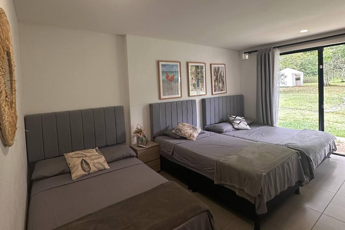 Quarto moderno com duas camas, uma janela grande e obras de arte na parede.