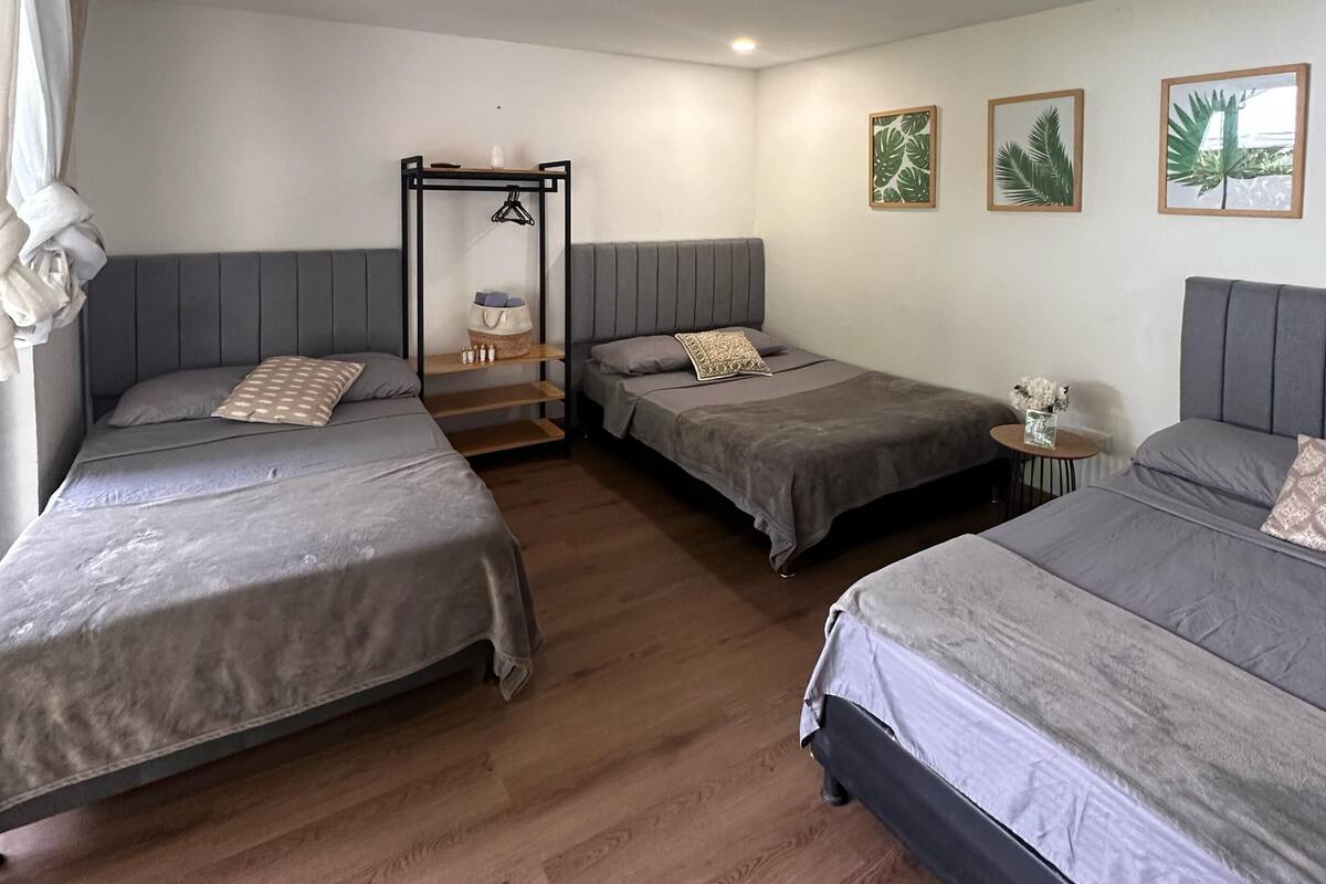 Quarto com quatro camas, uma mesinha e três quadros na parede.