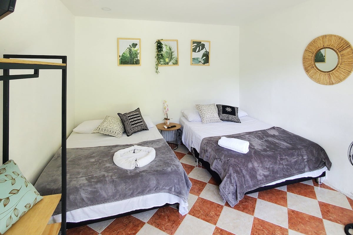 Quarto pequeno e limpo com duas camas, televisão e chão xadrez.