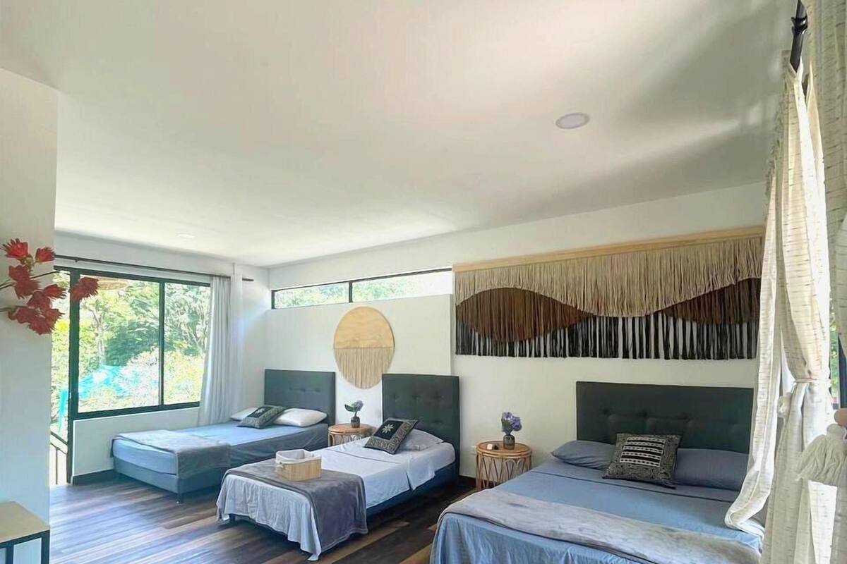 Quarto moderno com duas camas de solteiro, uma mesinha e uma janela grande.