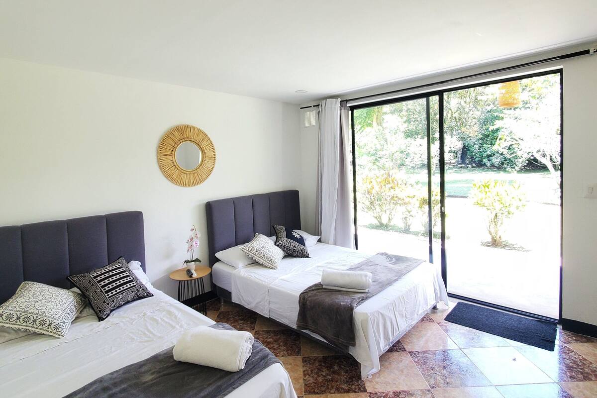 Quarto de hotel com duas camas, uma janela grande e vista para o exterior.