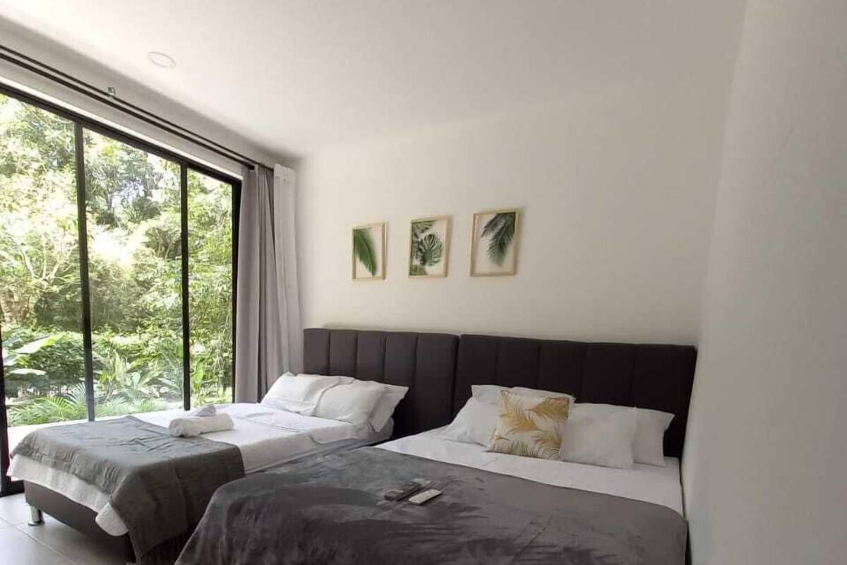 Quarto moderno com duas camas, janelas amplas e arte de parede com tema tropical.