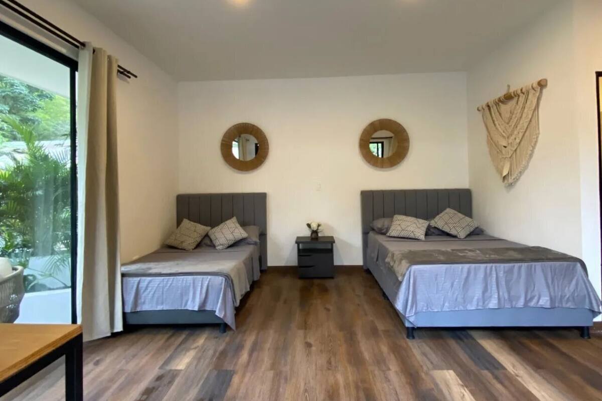Quarto moderno com duas camas, piso de madeira e uma mesinha.
