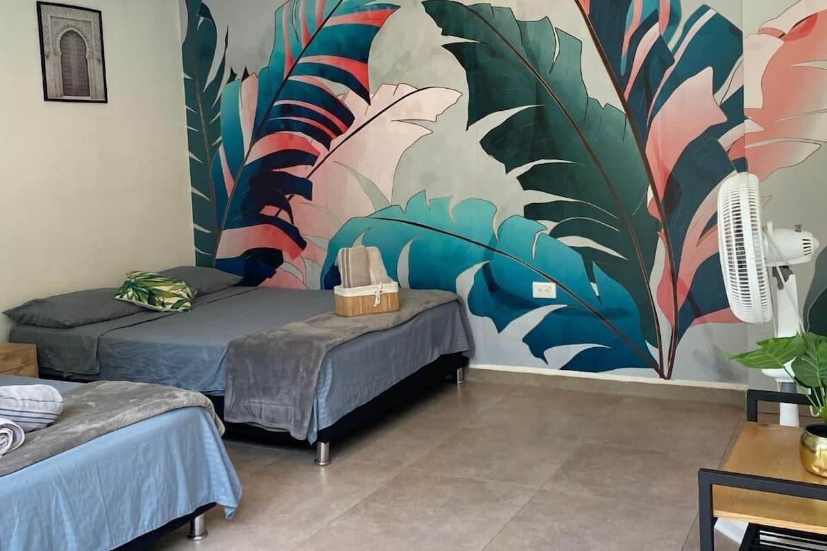 Quarto com duas camas, um grande mural na parede, um ventilador de teto e uma pequena mesa com uma planta.