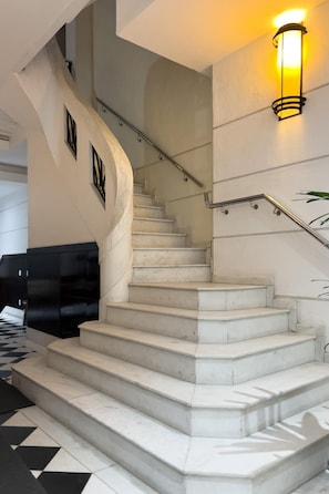 Un escalier en marbre, doté d’une rampe et d’un luminaire fixé au mur.