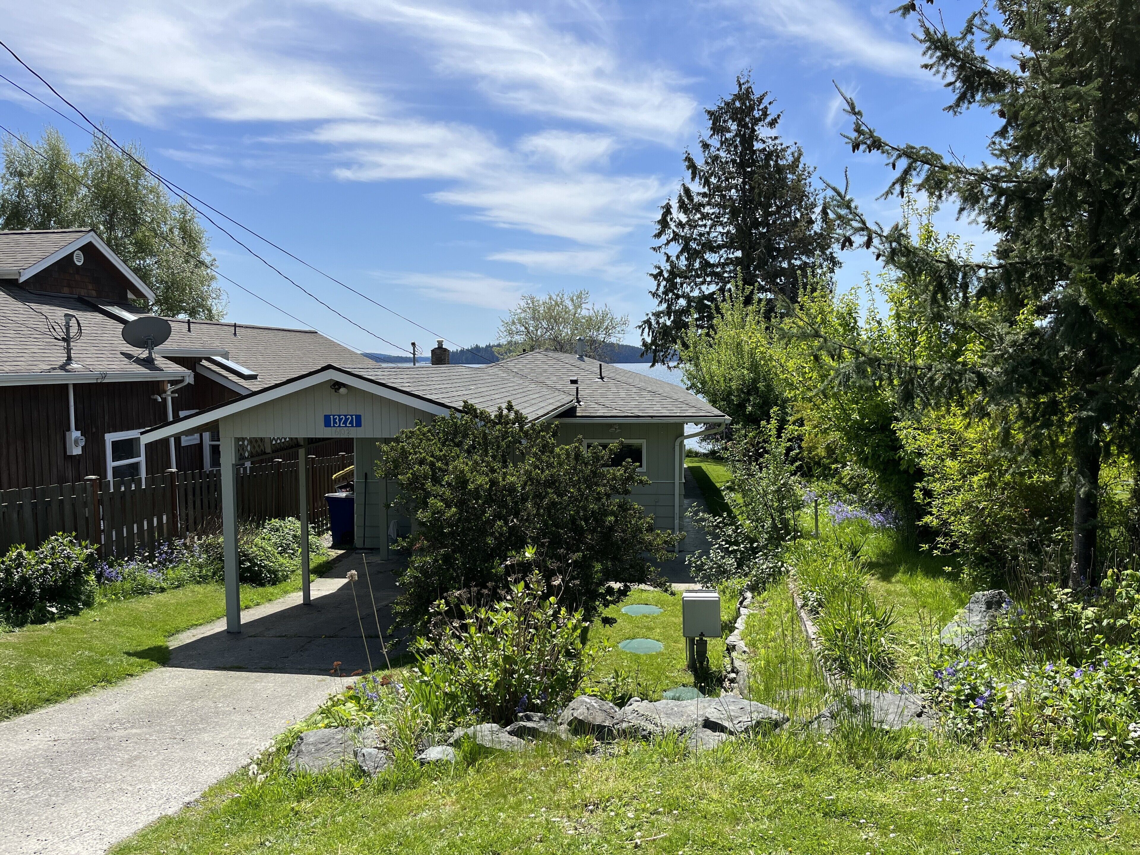 A small lodge with a covered entrance, a gravel path leading to the door, and a natural setting with trees and a pond.