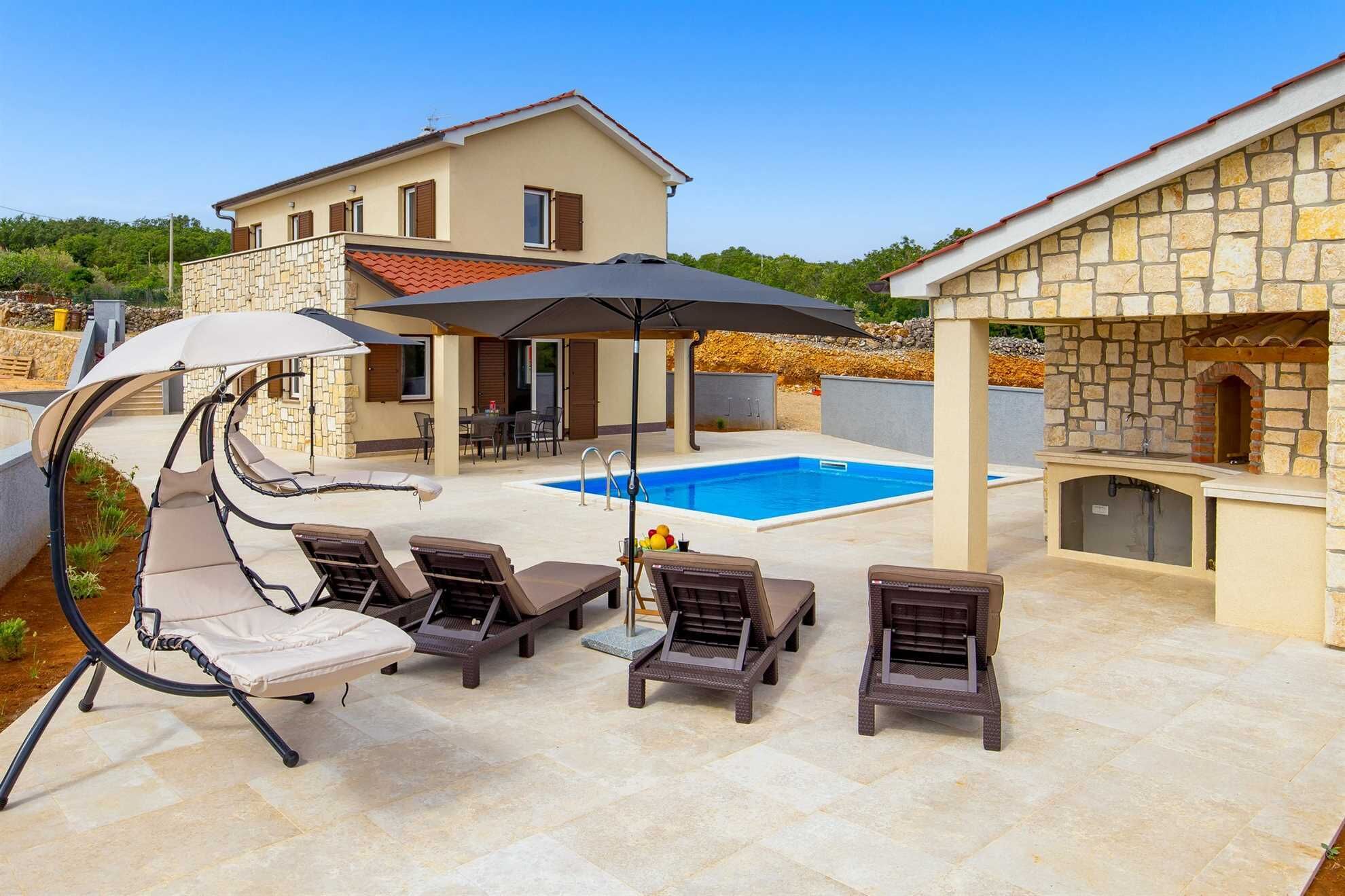 A poolside area with lounge chairs, a table, and a stone building with a fireplace.