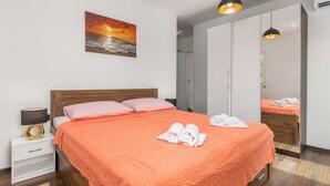 A modern hotel room with a large bed, a nightstand, a lamp, a painting of a sunset, and a wardrobe. - Villa Giulietta with a heated pool, fitness & Seaview (Vrbnik (Krk))