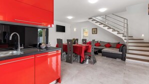 A modern kitchen with red cabinetry, a dining area with a red tablecloth, and a staircase leading to an upper level. - Villa Giulietta with a heated pool, fitness & Seaview (Vrbnik (Krk))
